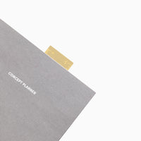 The Brass Bookmark Ruler peeking out of the Concept Planner on a white background.