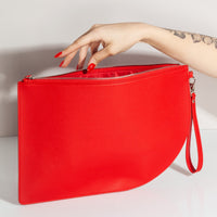 A hand holding a Poketo Red Curve Clutch on a white background. 